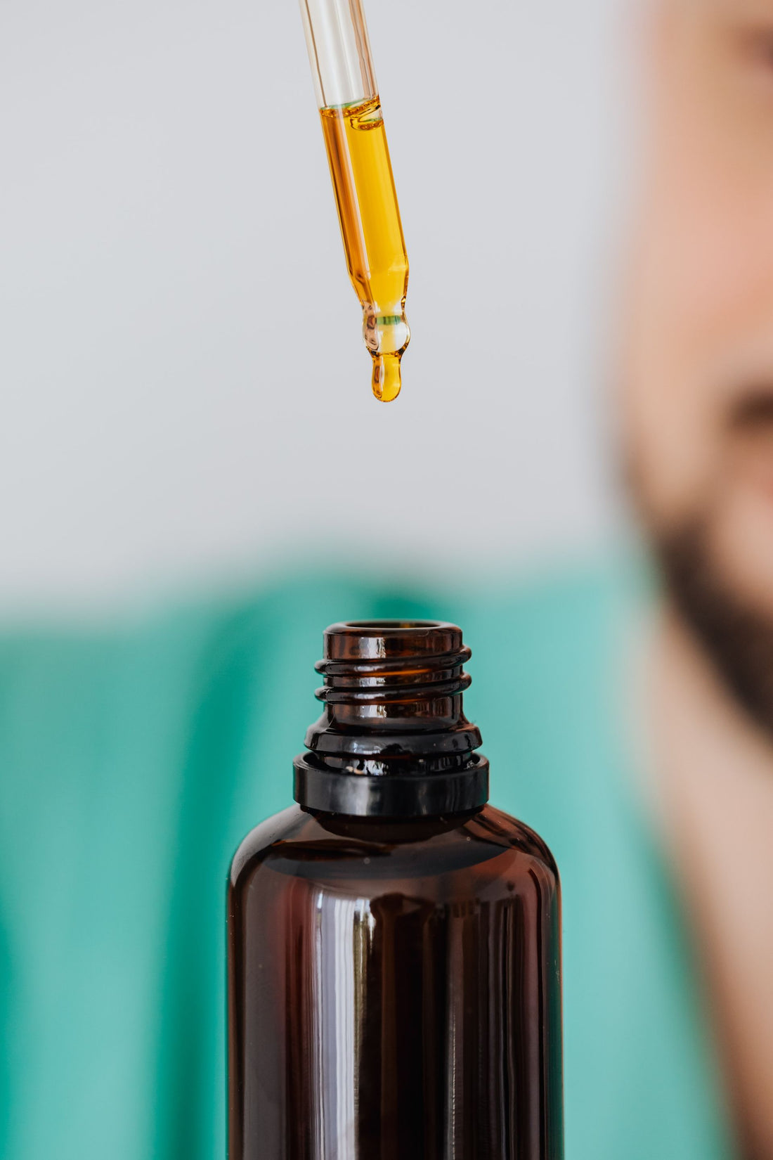 A dropper of golden tonic above an amber bottle — the daily StoneBlood ritual