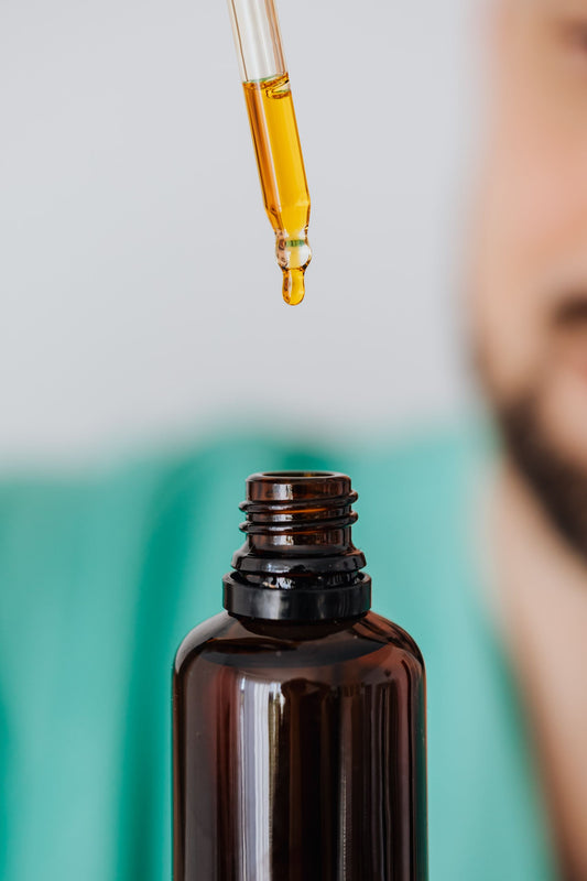 A dropper of golden tonic above an amber bottle — the daily StoneBlood ritual